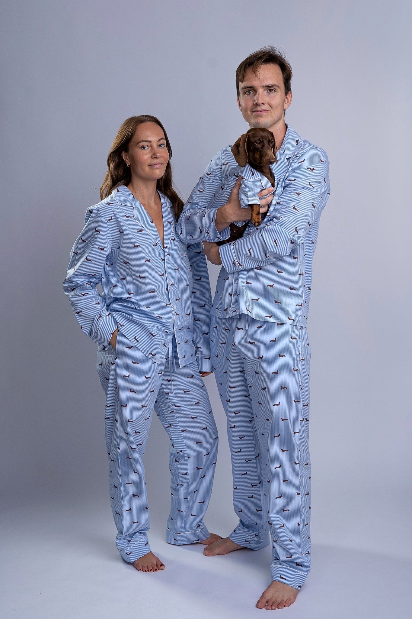 Man, woman and dachshund wearing matching white and blue striped pajamases with dachshund prints